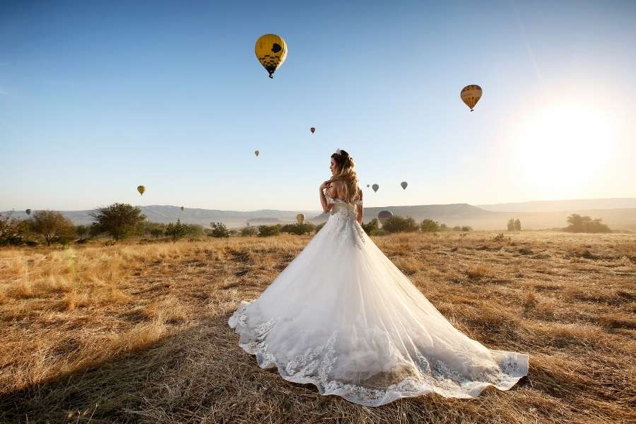 Mariée en robe longue dans un paysage avec montgolfières pour des photos de mariage