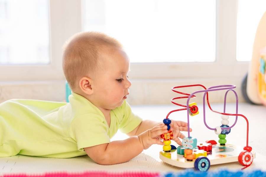 Un bébé allongé sur le ventre joue avec un labyrinthe de perles pour encourager la motricité fine.