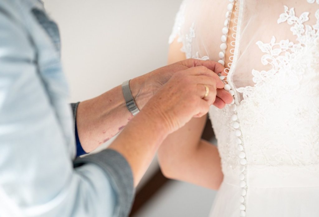 Une personne ajustant les boutons d'une robe en dentelle pour savoir que mettre dans la trousse de secours mariee le jour J